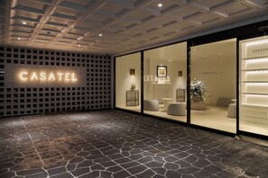 A modern hotel entrance with a stone-tiled floor, a glass facade, and the name 'CASATEL' illuminated on the wall.