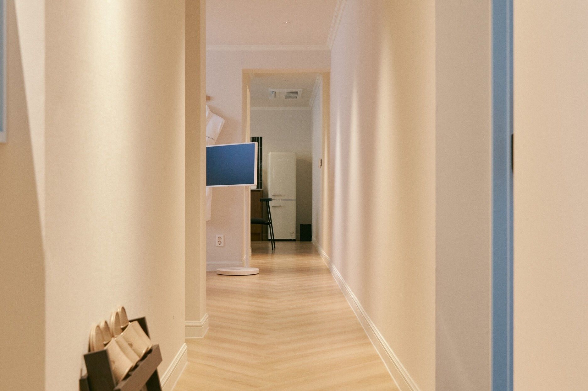 A hallway with a white refrigerator, a blue monitor, and a white door at the end.