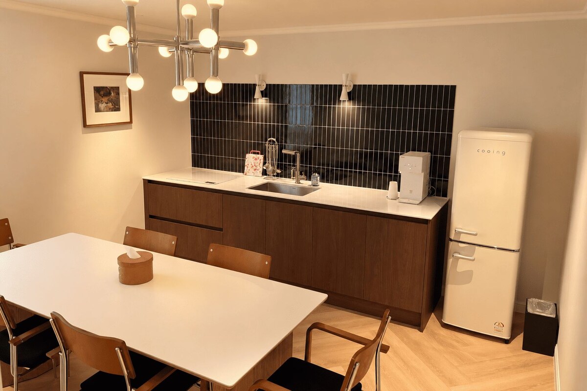 A modern kitchen with a white countertop, wooden cabinets, a black backsplash, and a white refrigerator.