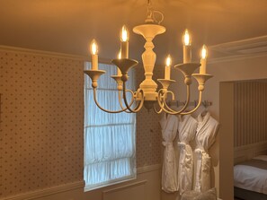 A room with a chandelier, a window with curtains, and a bed with a white comforter.