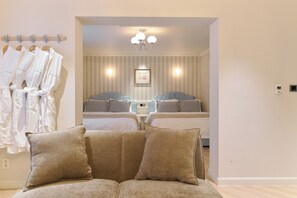 Una habitación de hotel con sofá, dos camas, un espejo y un perchero con batas.
