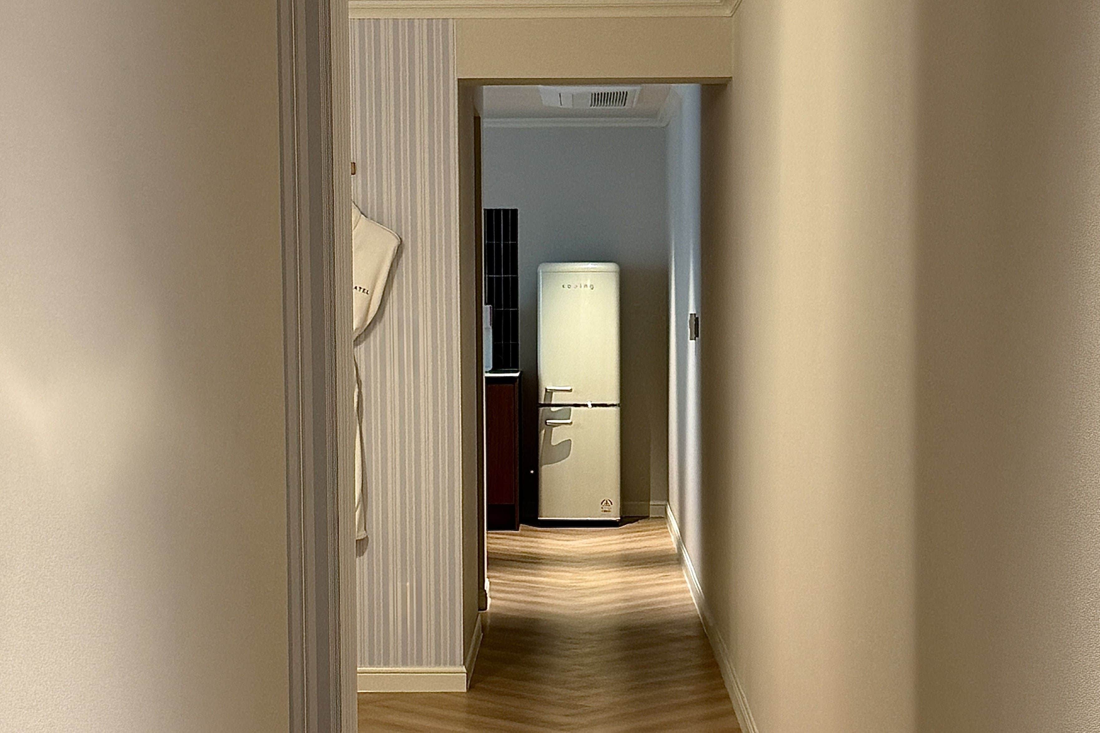 A narrow hallway with a refrigerator and a door on the right.