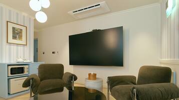A modern living room with a flat-screen TV mounted on the wall, two armchairs, a coffee table, and a built-in microwave.