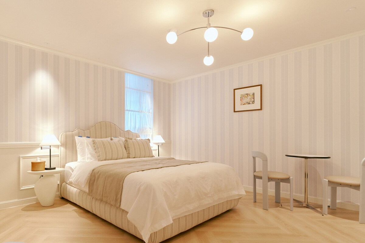 A bedroom with a bed, bedside tables, a chair, a small table, and a picture on the wall.