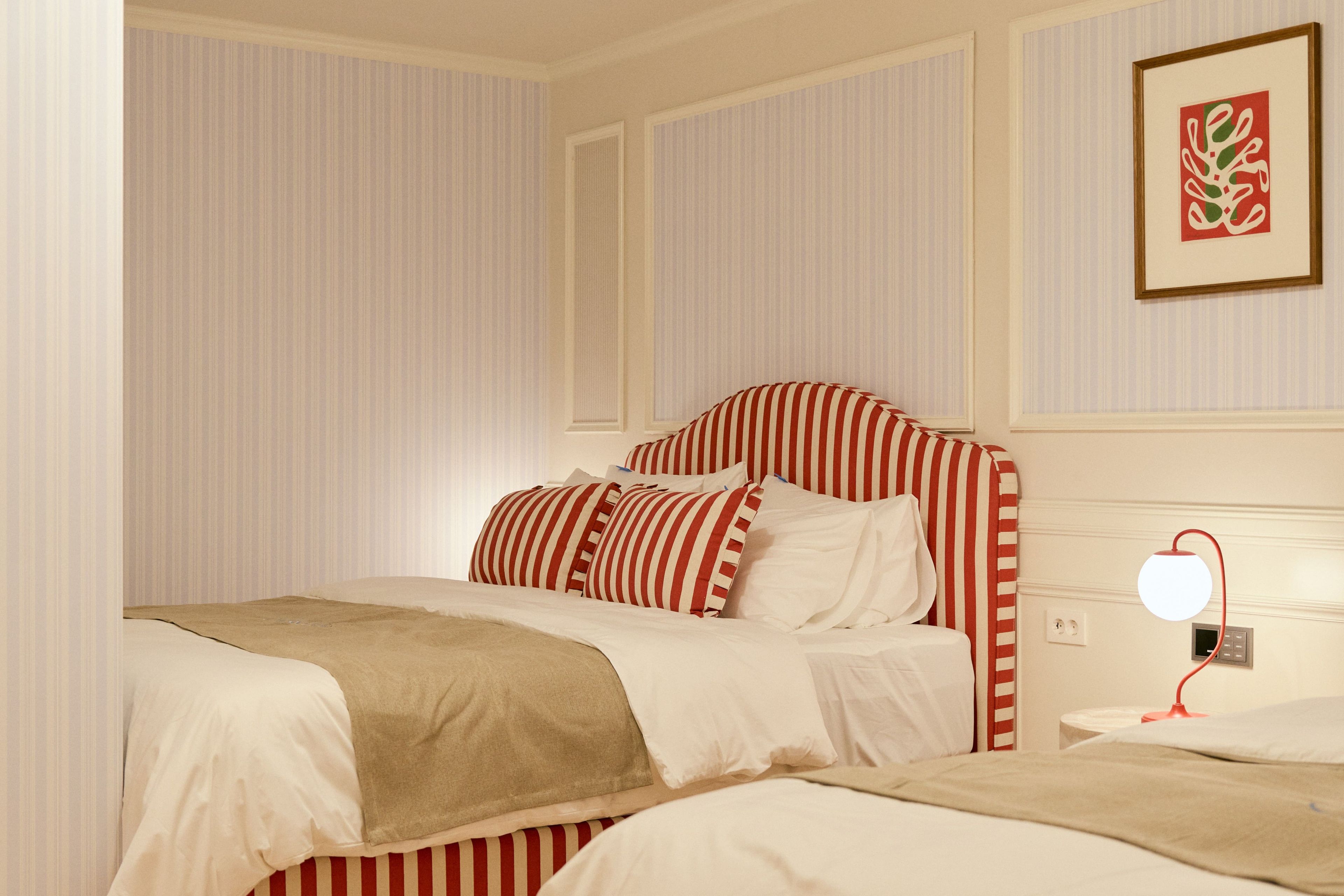 A hotel room with a striped bed, a bedside table with a lamp, and a framed picture on the wall.