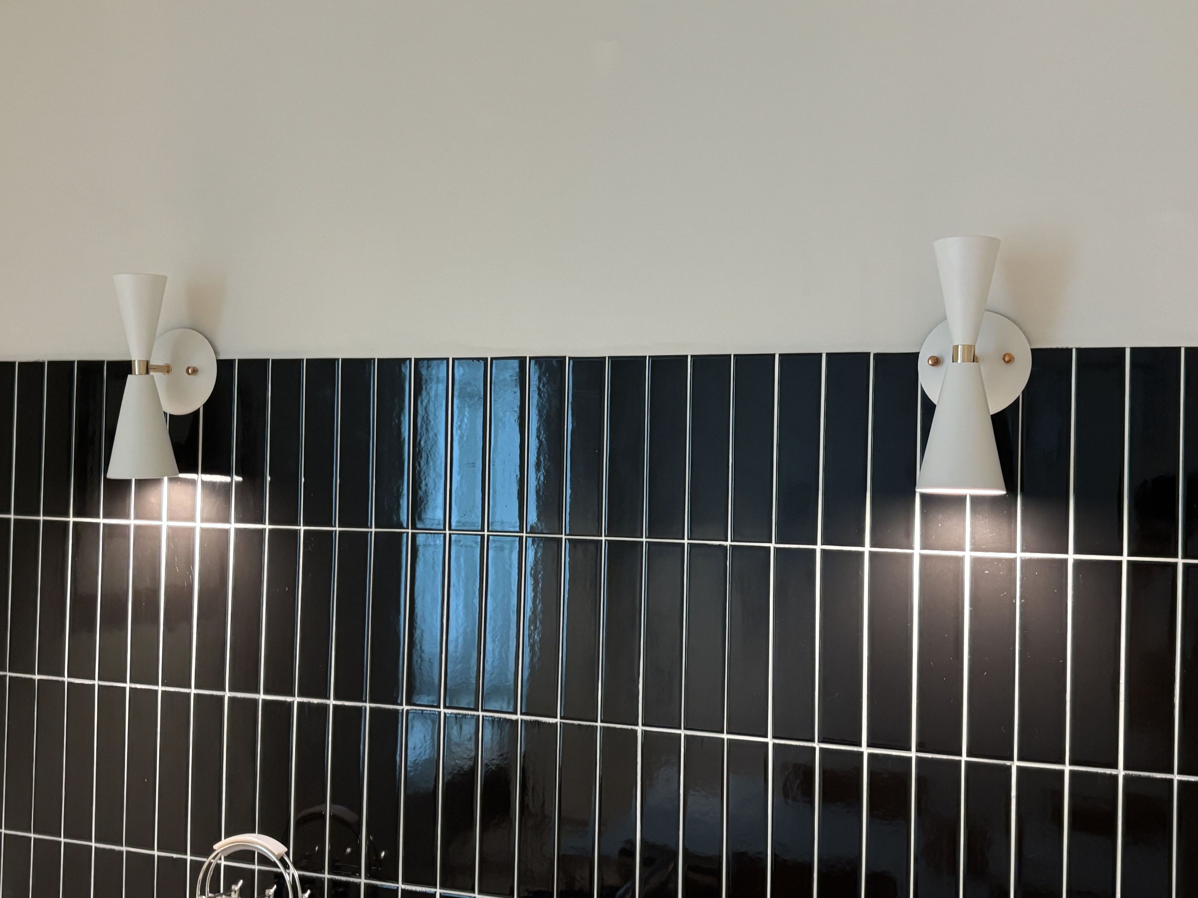 Un baño con paredes cubiertas de mosaicos blancos y negros, dos luminarias empotradas y una instalación de fontanería visible.