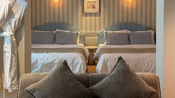 Quarto de hotel com duas camas, área de estar com uma poltrona e almofadas, roupão pendurado e quadro na parede.
