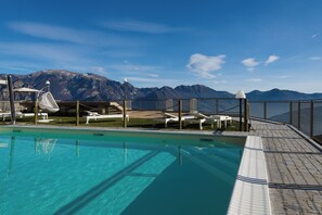 Piscina con sillones de descanso y vistas a montañas.