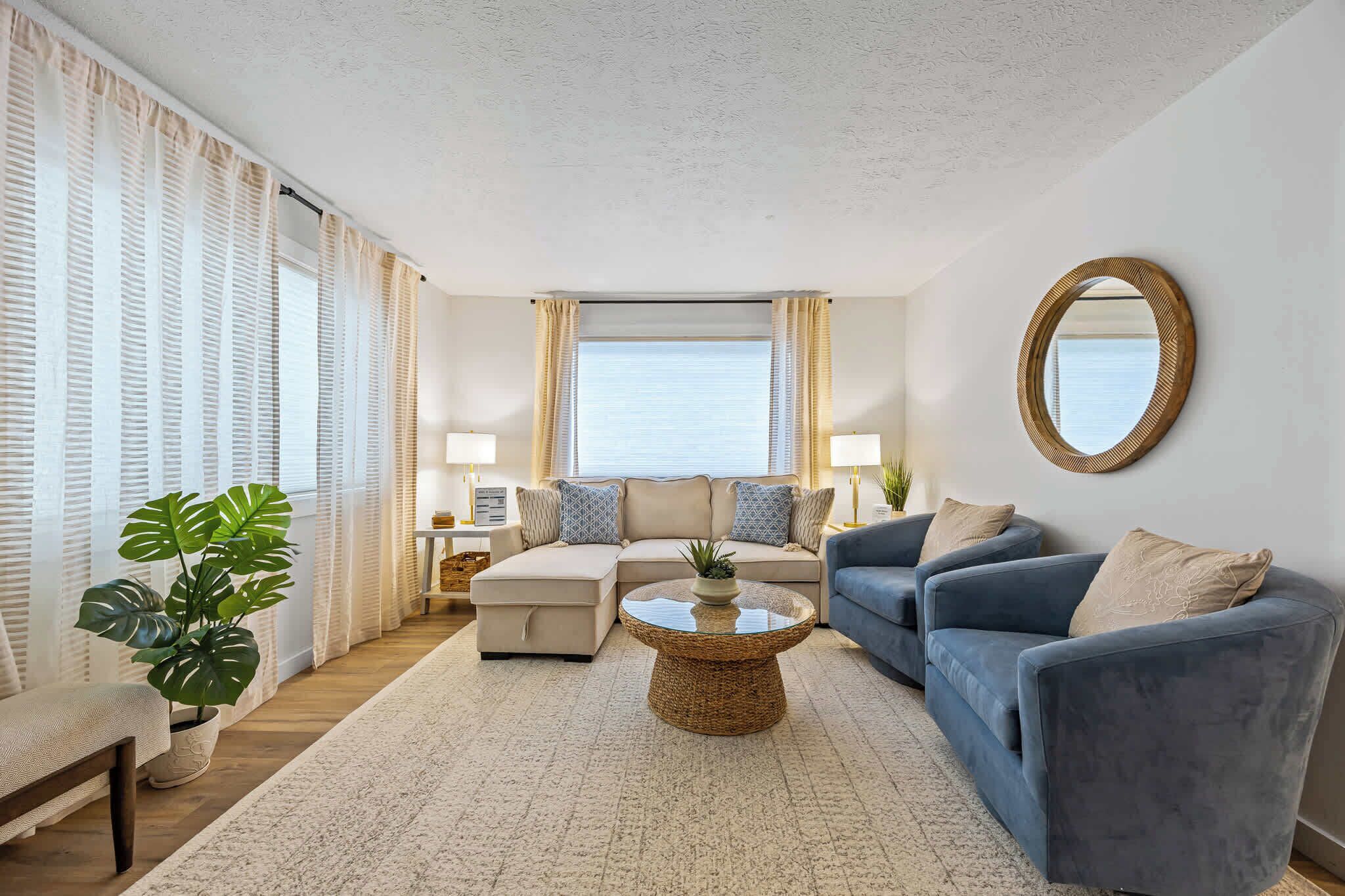 A living room with a sofa, armchair, coffee table, and a potted plant.