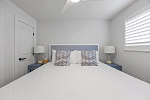 Ein Schlafzimmer mit einem Bett, zwei Nachttischen mit Lampen, einer Tür und einem Fenster mit Jalousien.