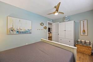 Ein Schlafzimmer mit einem Bett, einem Deckenventilator, einem Gemälde mit Segelbooten, einem Kleiderschrank und einem an der Wand befestigten Surfbrett.