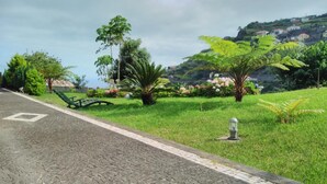 A paved pathway with a bench, surrounded by lush greenery and flowering plants. - Villa 'Quinta Do Serrado' with Sea View, Private Garden and Wi-Fi (Ribeira da Janela)
