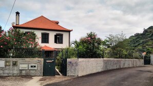 A two-story house with a red-tiled roof, a gated entrance, and a stone wall. - Villa 'Quinta Do Serrado' with Sea View, Private Garden and Wi-Fi (Ribeira da Janela)