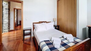 A hotel room with a wooden bed, a nightstand, a lamp, and a checkered bedspread. - Villa 'Quinta Do Serrado' with Sea View, Private Garden and Wi-Fi (Ribeira da Janela)