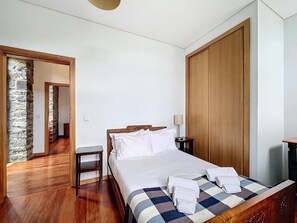 A hotel room with a wooden bed, a nightstand, a lamp, and a checkered bedspread. - Villa 'Quinta Do Serrado' with Sea View, Private Garden and Wi-Fi (Ribeira da Janela)