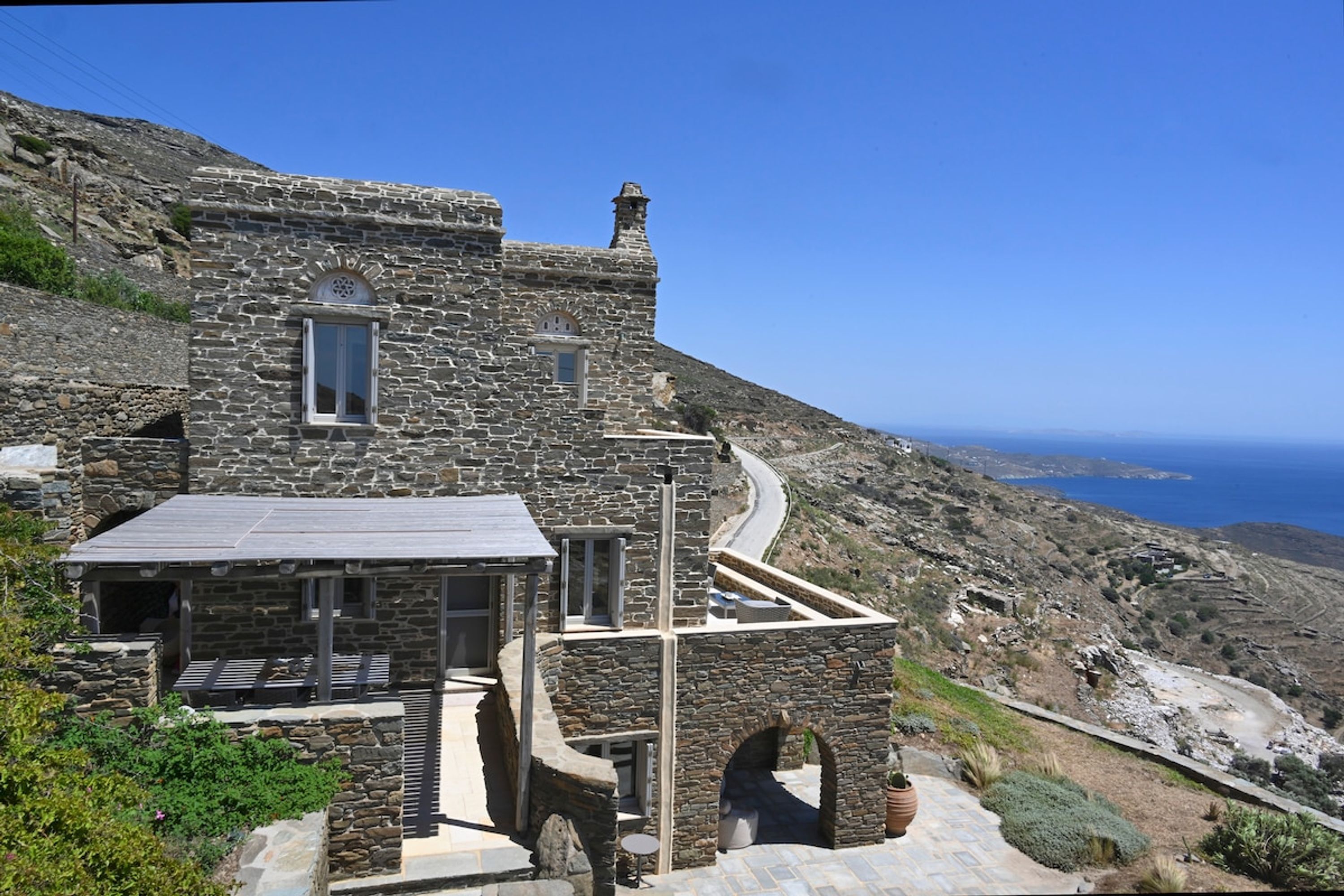 Ein Steinhaus mit Terrasse, einem kleinen Fenster und Blick auf das Meer.