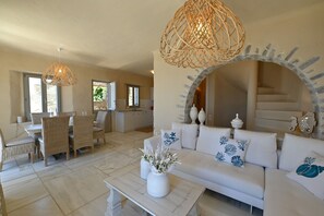 Ein geräumiger Wohnbereich mit einem weißen Sofa, einem Esstisch und Stühlen, einer Küche im Hintergrund und einem großen, bogenförmigen Durchgang.