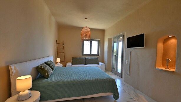 Un dormitorio con cama, mesitas de noche, lámpara colgante, televisor y ventana.