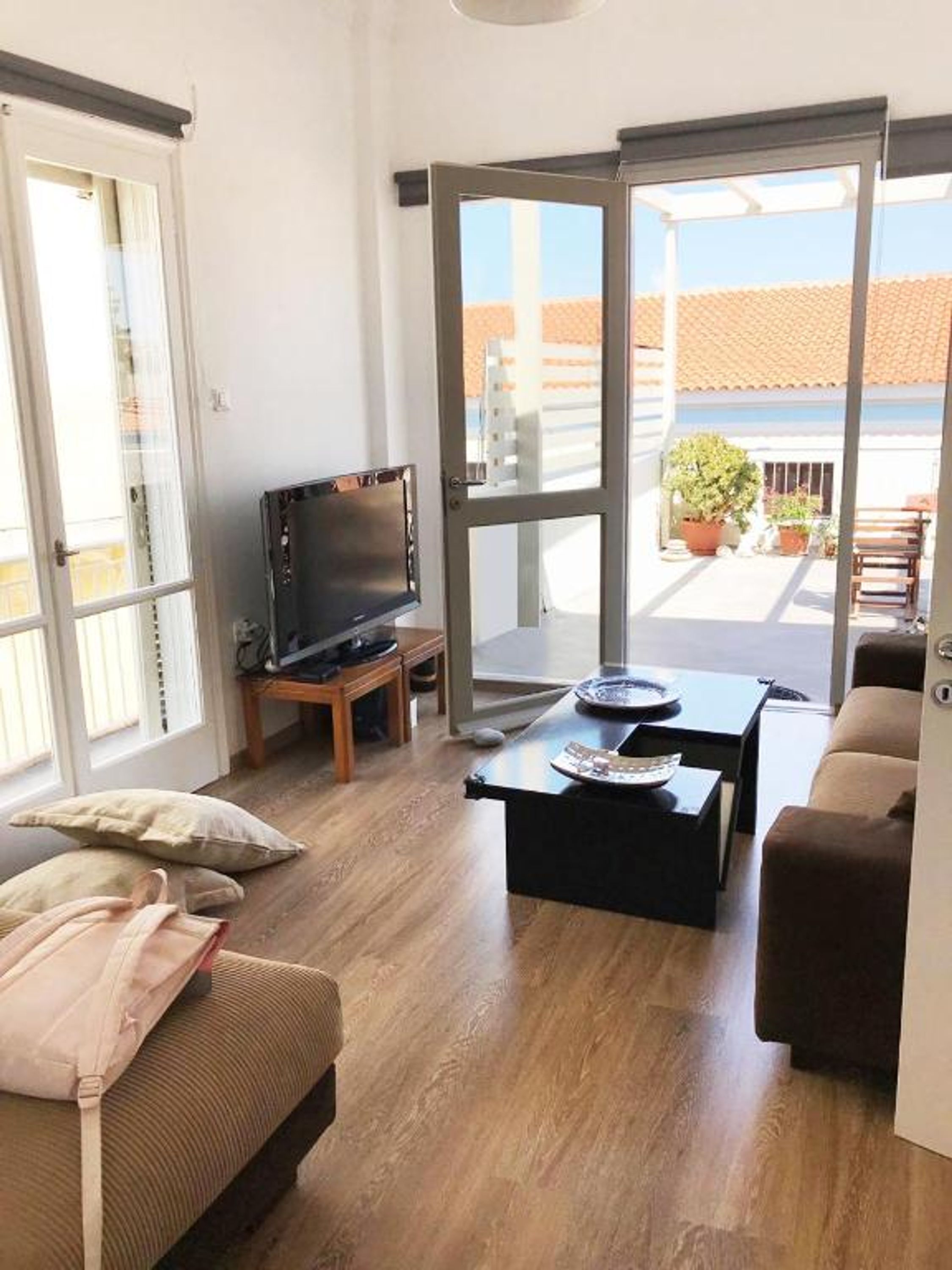 Un soggiorno con divano, tavolino, televisione e una porta scorrevole in vetro che dà su un'area esterna con piante in vaso.