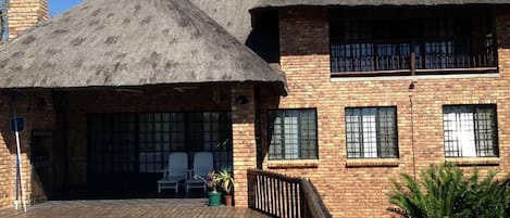 A two-story building with a thatched roof, a swimming pool, and a deck area with chairs.