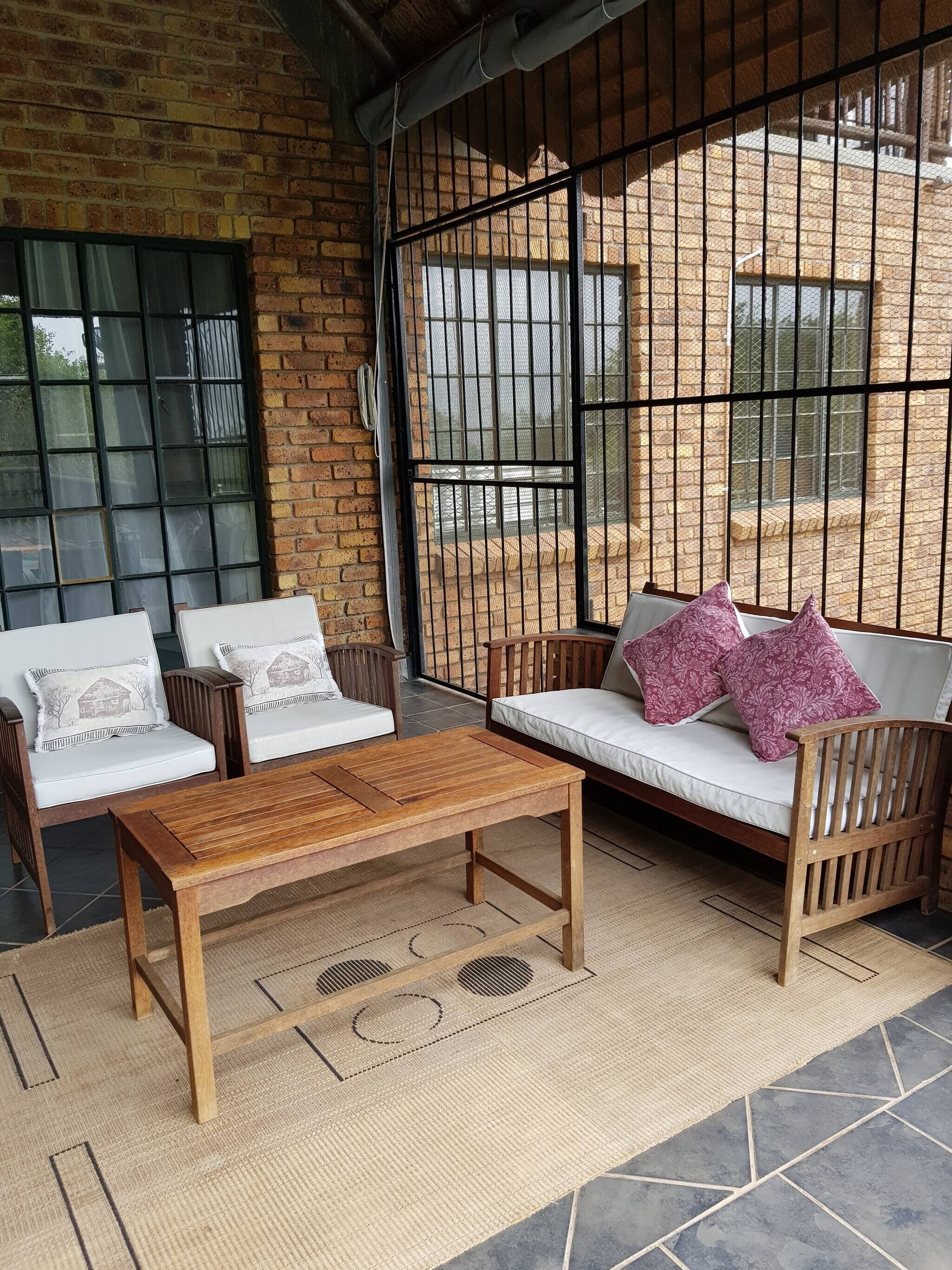 A room with a brick wall, a wooden table, two sofas with patterned cushions, and a large window with metal bars.