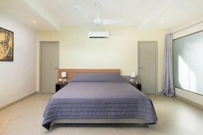 Un dormitorio ordenado con cama, ventilador de techo, aire acondicionado y ventana con cortinas.