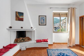 Ein Wohnzimmer mit Kamin, einem gerahmten Bild, einem Fenster mit Blick auf Gebäude und einem gemusterten Teppich.