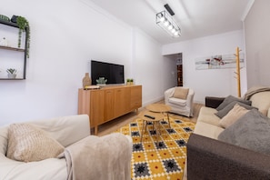 A living room with a sofa, armchair, coffee table, TV, and a painting on the wall. - Alma Canteras Vacation Apartment with Sea Views and Wi-Fi (Las Palmas de Gran Canaria)