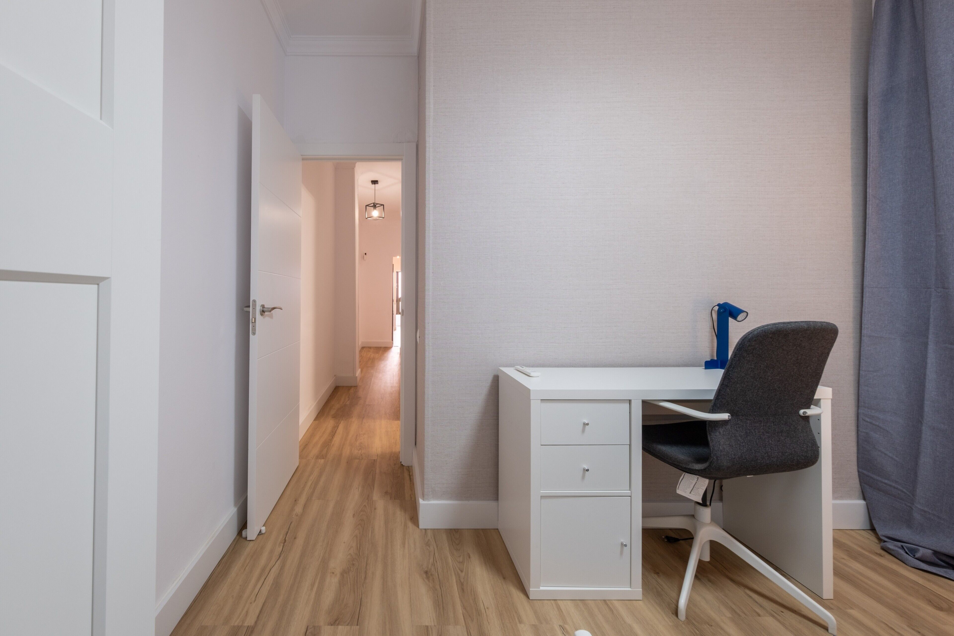 A room with a white desk, a grey chair, and a white wardrobe.