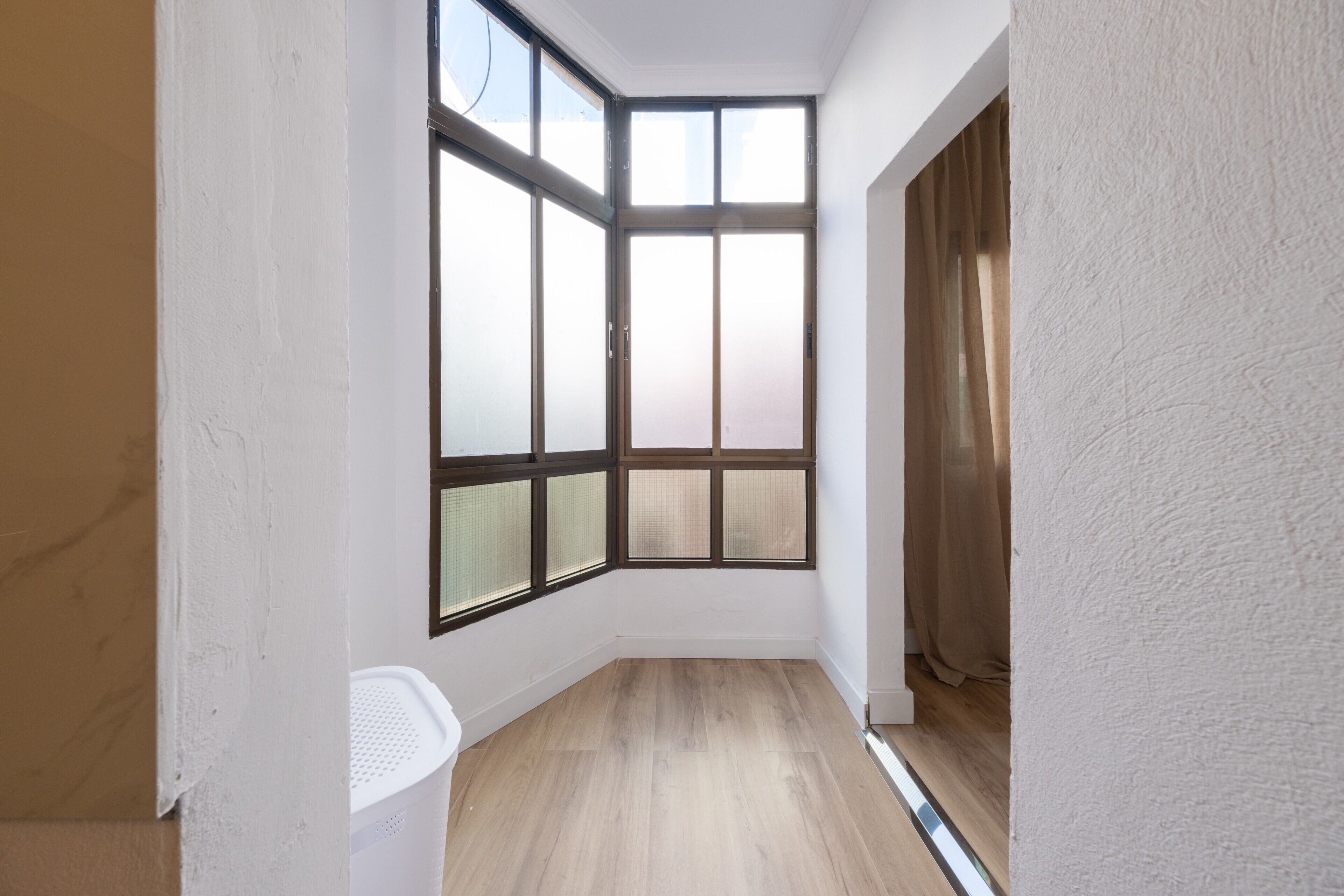 A room with a corner window, wooden flooring, and white walls.