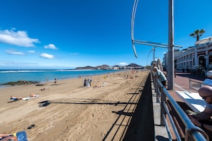 A beach with people sunbathing and swimming, a clear sky, and buildings in the background. - Alma Canteras Vacation Apartment with Sea Views and Wi-Fi (Las Palmas de Gran Canaria)