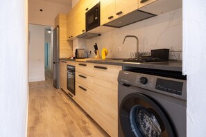 A modern kitchen with wooden cabinets, a built-in oven, a dishwasher, and a front-loading washing machine. - Alma Canteras Vacation Apartment with Sea Views and Wi-Fi (Las Palmas de Gran Canaria)