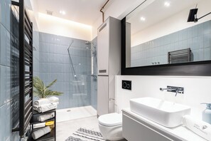 Un baño moderno con cabina de ducha de vidrio, lavabo blanco y retrete.