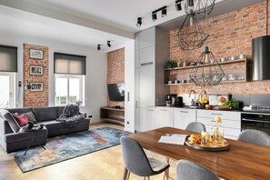 Una cocina moderna con pared de ladrillo, armarios blancos y un comedor con mesa y sillas de madera.