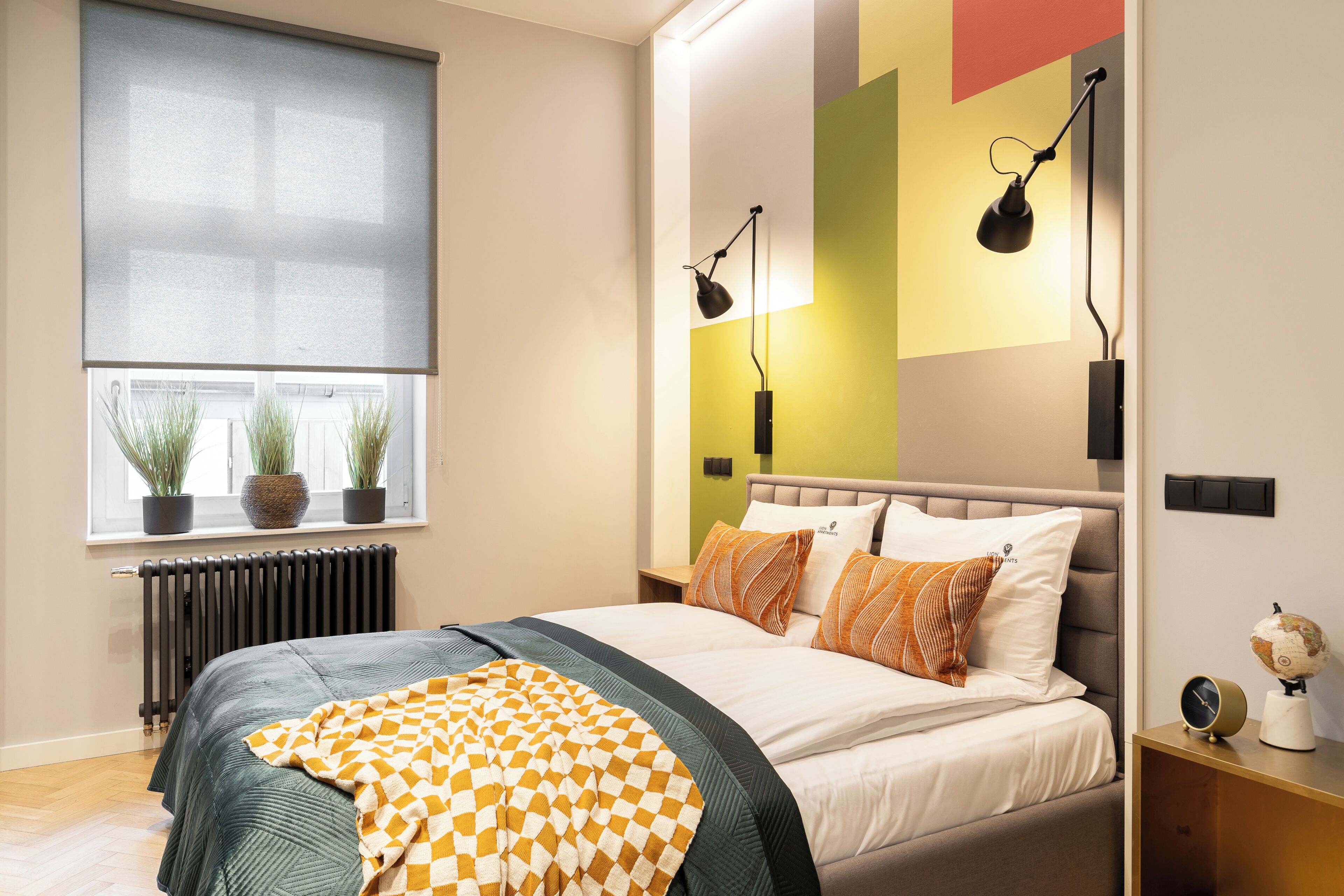 Une chambre à coucher moderne avec un lit, des lampes de chevet, un radiateur, une fenêtre avec des plantes et un globe sur la table de chevet.