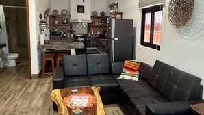 Un espacio habitable compacto con cocina, un sofá de cuero negro, una mesa de centro de madera y un tapete estampado.
