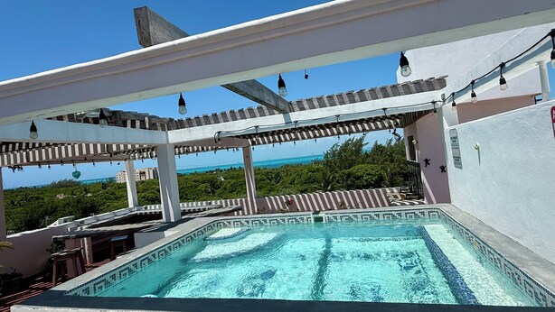 Una piscina en la azotea con vista al océano, rodeada por una pérgola con luces colgantes.
