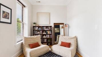 Una habitación con dos sillones color beige, una estantería, un espejo y una alfombra estampada.