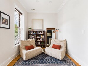 A room with two beige armchairs, a bookshelf, a mirror, and a patterned rug.
