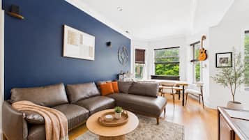 Ein modernes Wohnzimmer mit einer Eckcouch, einem runden Couchtisch und einem großen Fenster mit Jalousien.