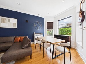 A modern living room with a blue accent wall, a wooden dining table, and a gray sofa.