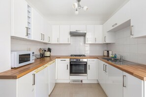 Cozinha moderna com armários brancos, micro-ondas, fogão e lava-louças.