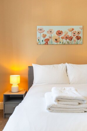 A hotel room with a bed, a bedside lamp, and a painting of flowers on the wall. - GuestReady - Charming Kingston Home with Garden (London)