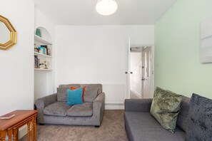 A living room with a grey sofa, a wooden side table, and a bookshelf. - GuestReady - Charming Kingston Home with Garden (London)