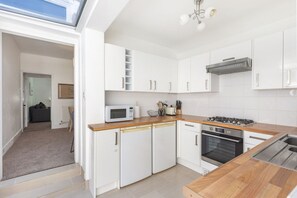 A modern kitchen with white cabinets, a microwave, a toaster, and a stove. - GuestReady - Charming Kingston Home with Garden (London)