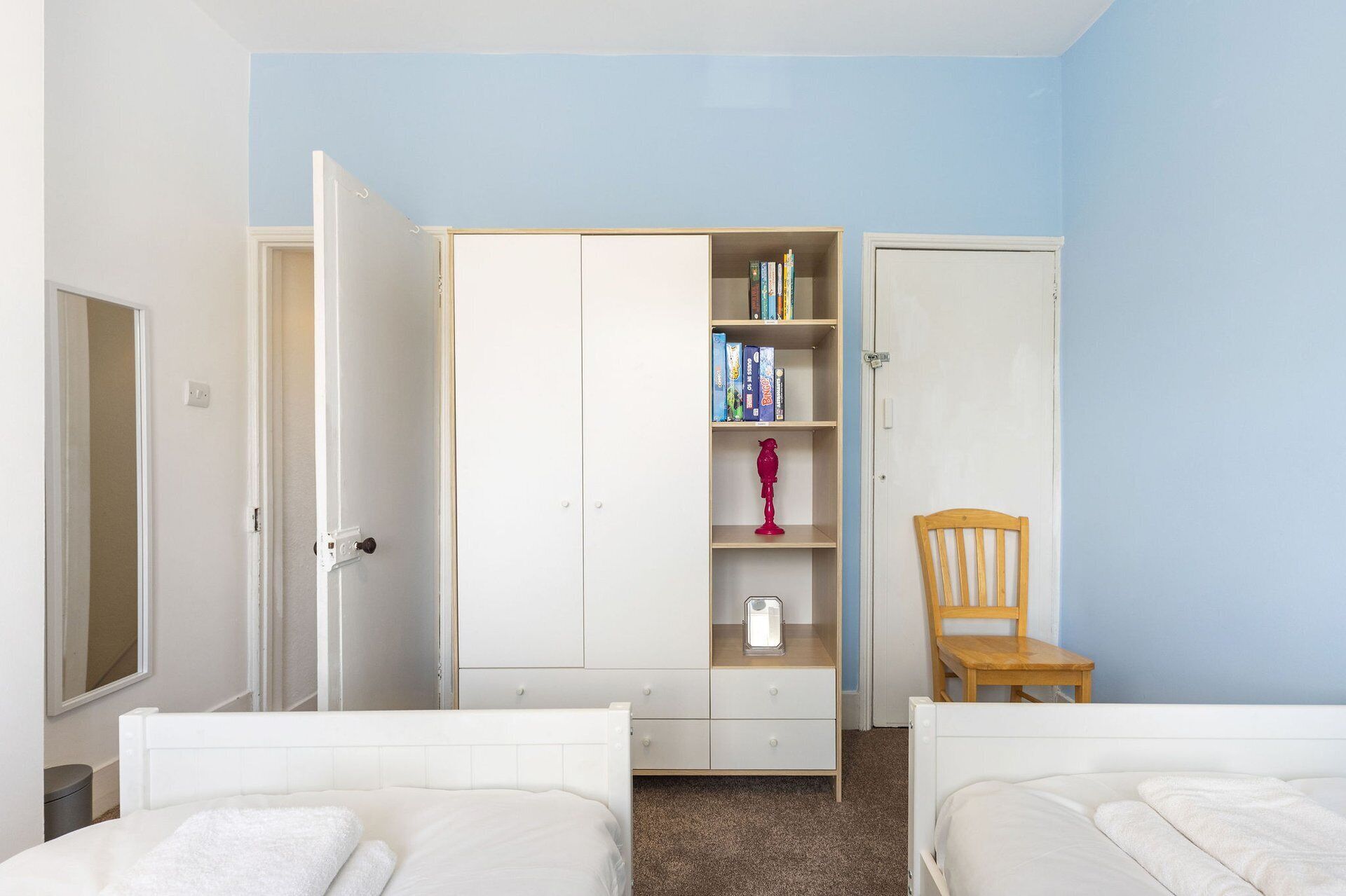 Un dormitorio con dos camas, un armario, una silla y una estantería.