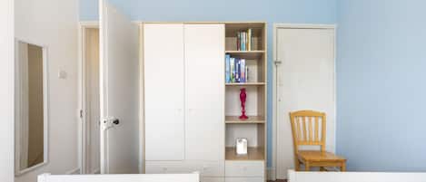 Un dormitorio con dos camas, un armario, una silla y una estantería.