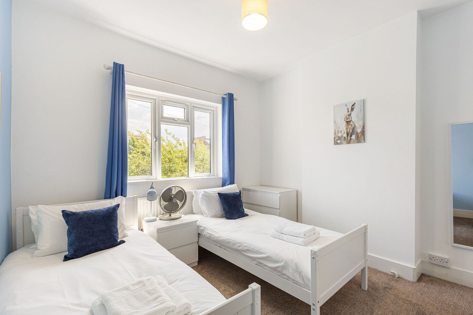 A bedroom with two single beds, a bedside table with a lamp, a radiator, and a window with curtains.
