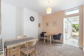 A room with a wooden table, two chairs, a clock, and a window with a view of the outdoors. - GuestReady - Charming Kingston Home with Garden (London)
