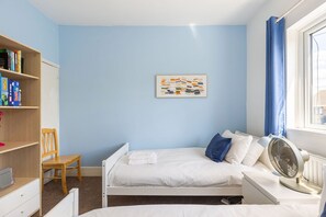 A bedroom with a bed, a chair, a bookshelf, a radiator, and a window with curtains. - GuestReady - Charming Kingston Home with Garden (London)